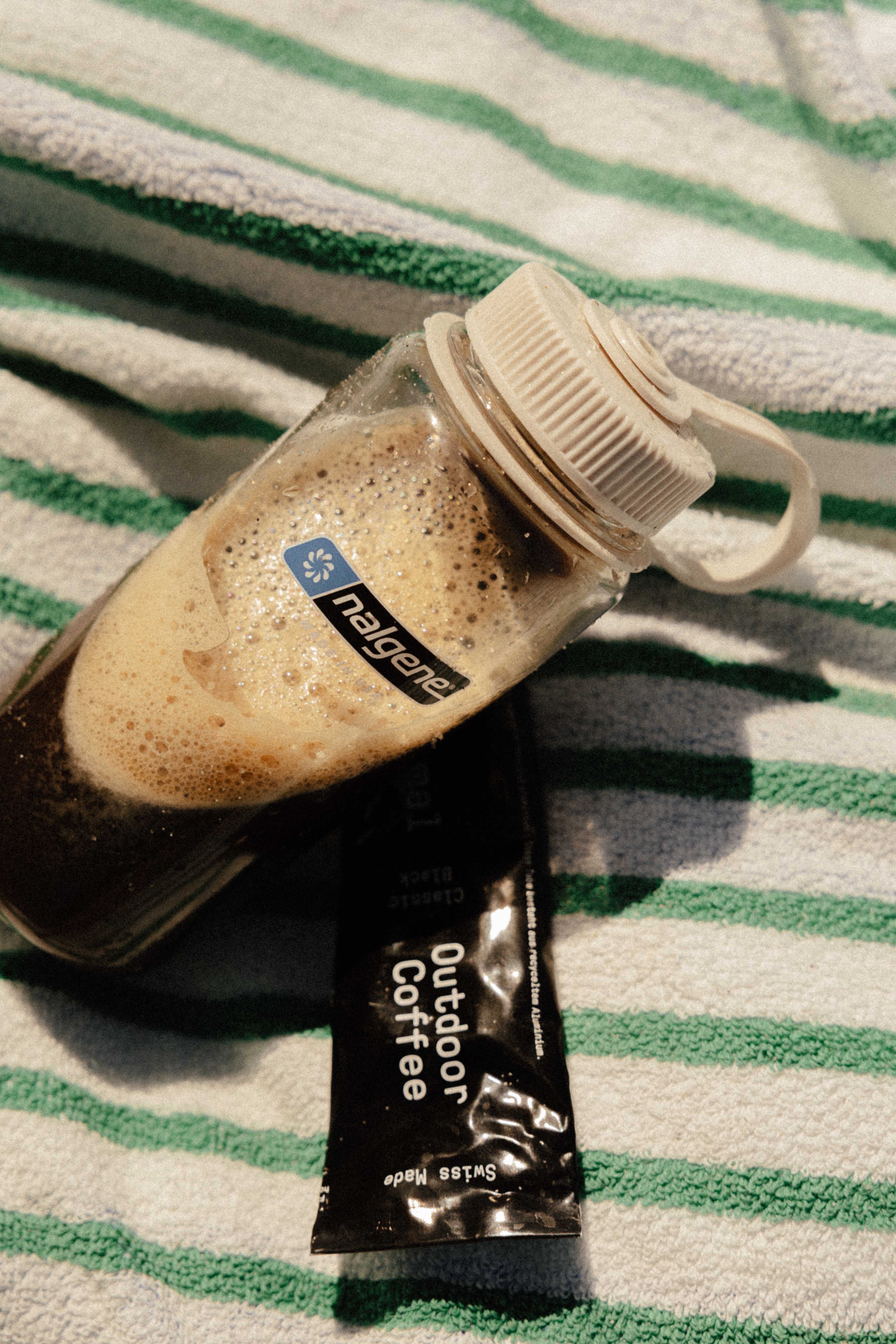 NoNormal Nalgene bottle with cold-mixed coffee next to a tube on a beach towel