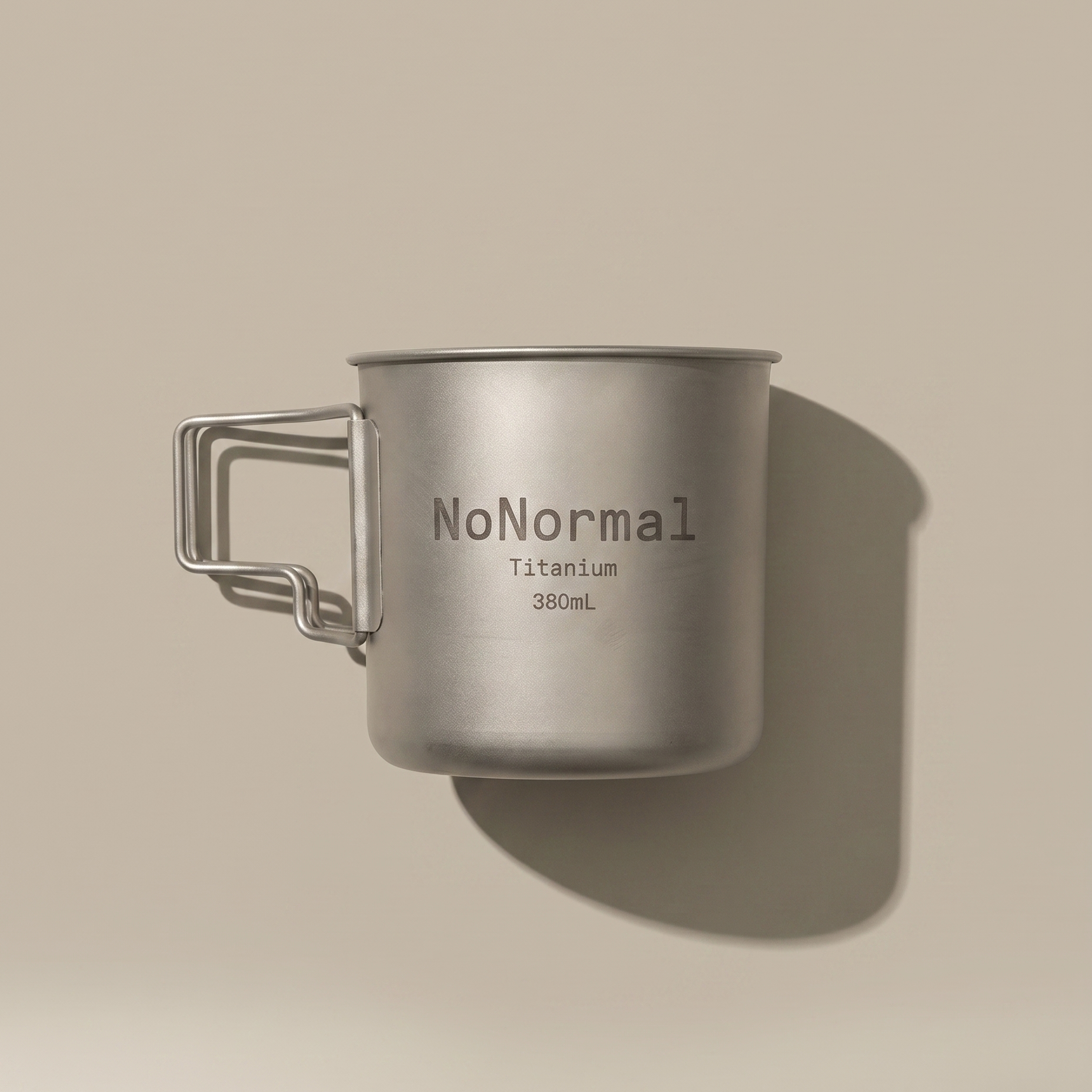 A titanium camping mug with a handle, featuring the text 'NoNormal Titanium 380mL' printed on its side, set against a solid beige background with a soft shadow.