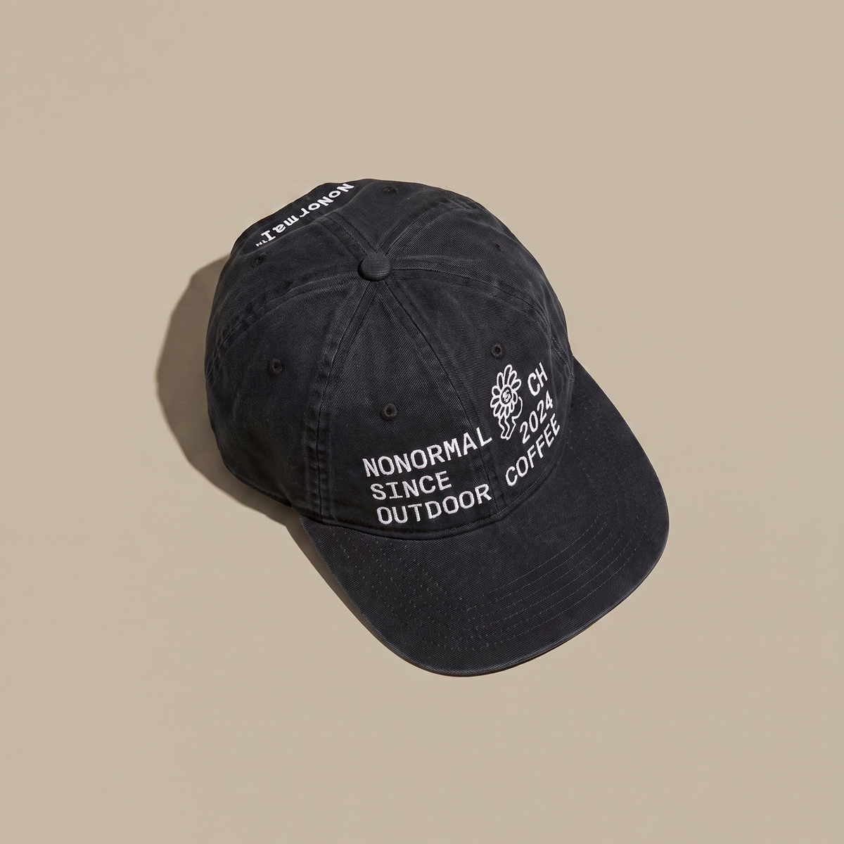 A dark washed baseball cap with white embroidered text reading 'NONORMAL OUTDOOR COFFEE' and a small logo on the front, photographed on a plain beige background.