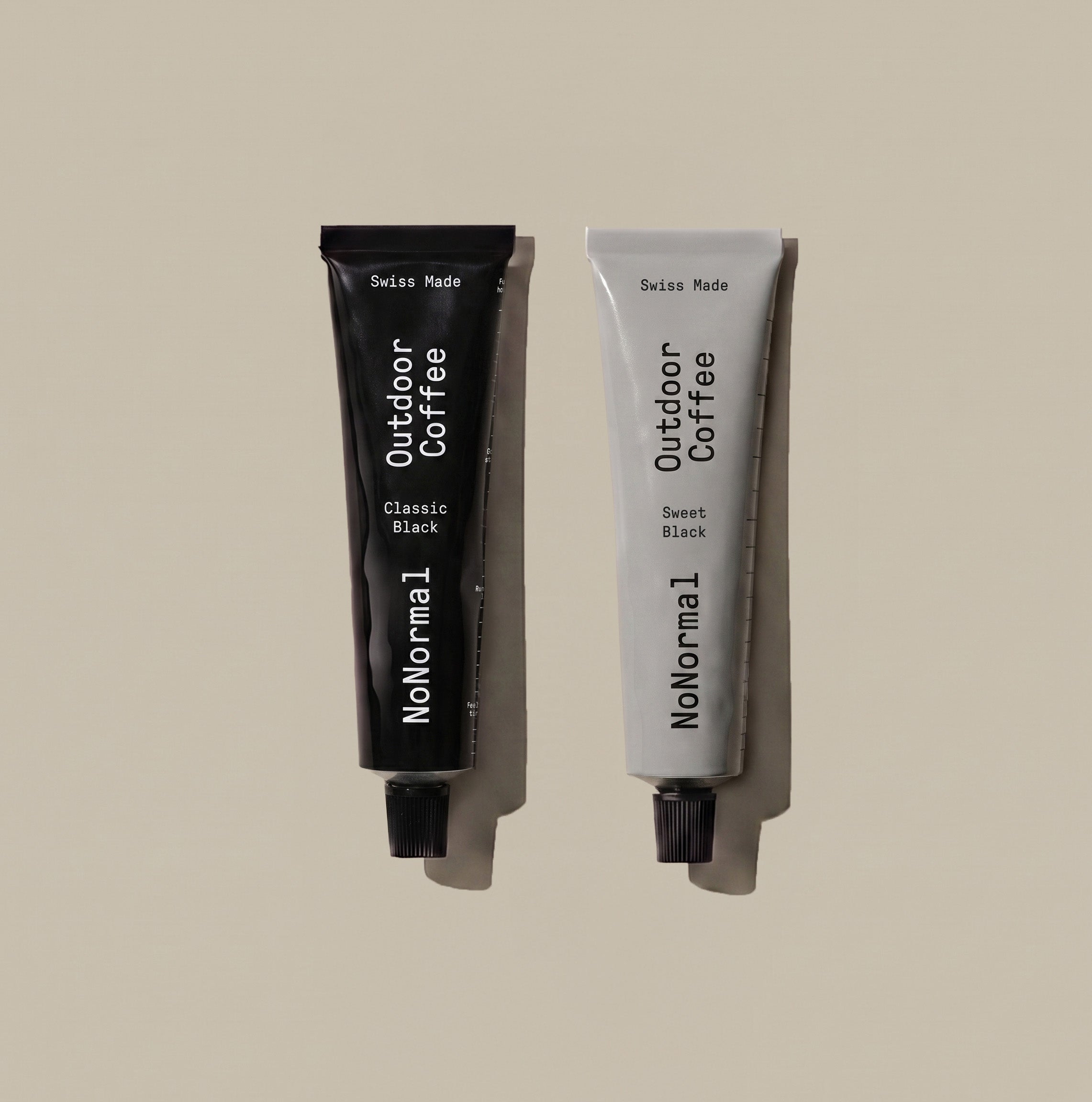 One NoNormal Classic Black and one Sweet Black tube side by side on a warm beige background.