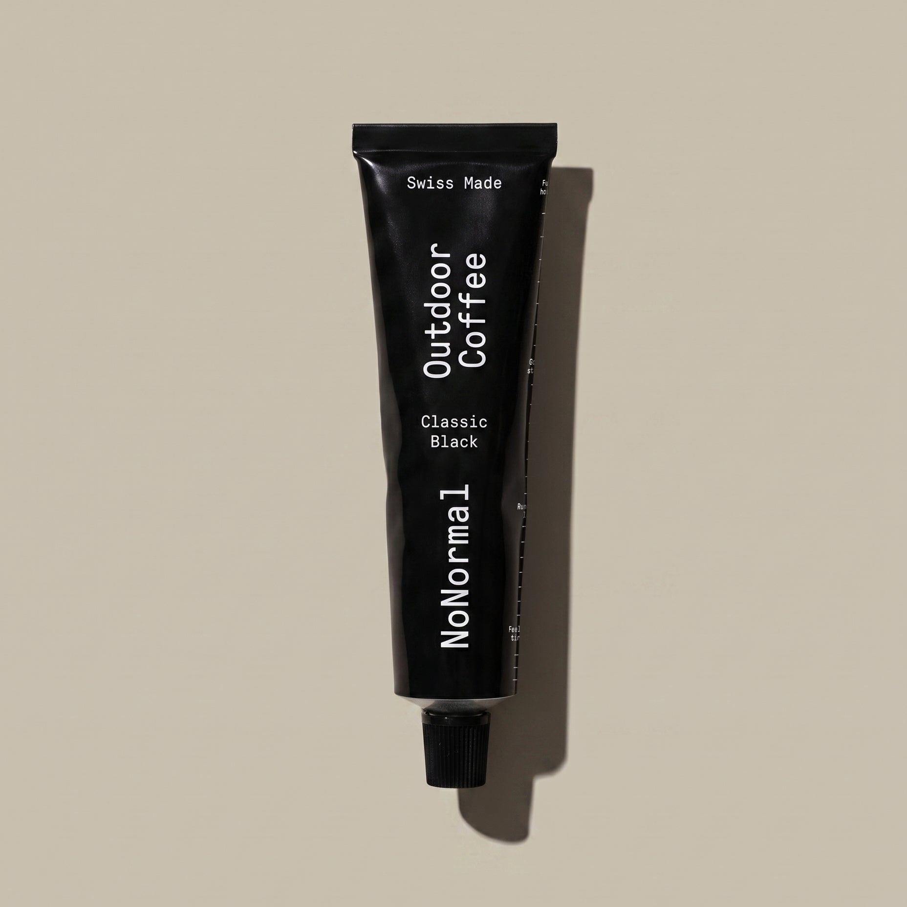 A black squeeze tube of NoNormal Outdoor Coffee Classic Black, standing vertically against a solid beige background with a soft shadow.