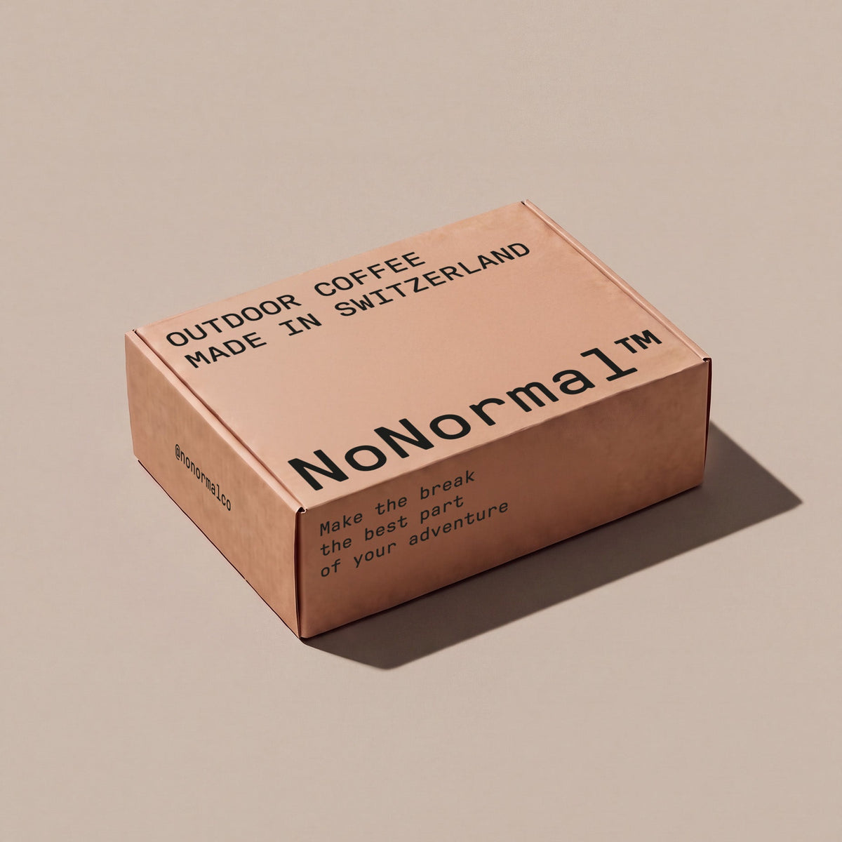 A square cardboard box in a warm tan or kraft-paper color, printed with black text including 'NoNormal' and 'OUTDOOR COFFEE MADE IN SWITZERLAND', photographed on a plain beige background with a soft shadow.