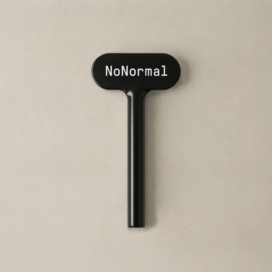 Black NoNormal tube squeeze key standing upright on a warm beige background.