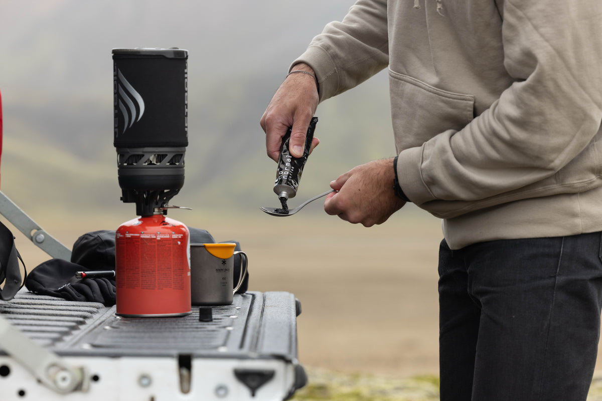 Squeezing NoNormal coffee paste into a cup beside a camping stove