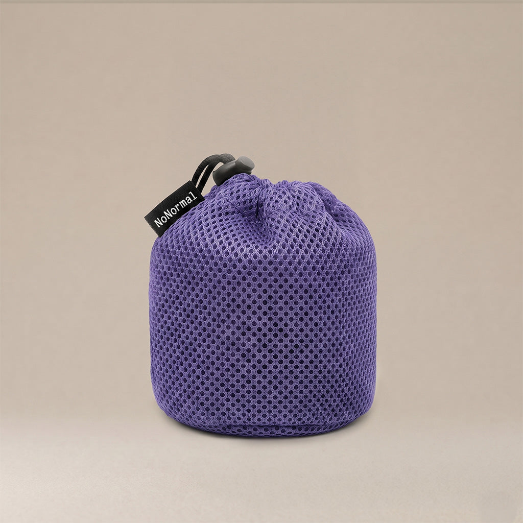 A purple mesh drawstring pouch with a black drawstring and a black fabric tag reading 'NoNormal' on a warm beige background.