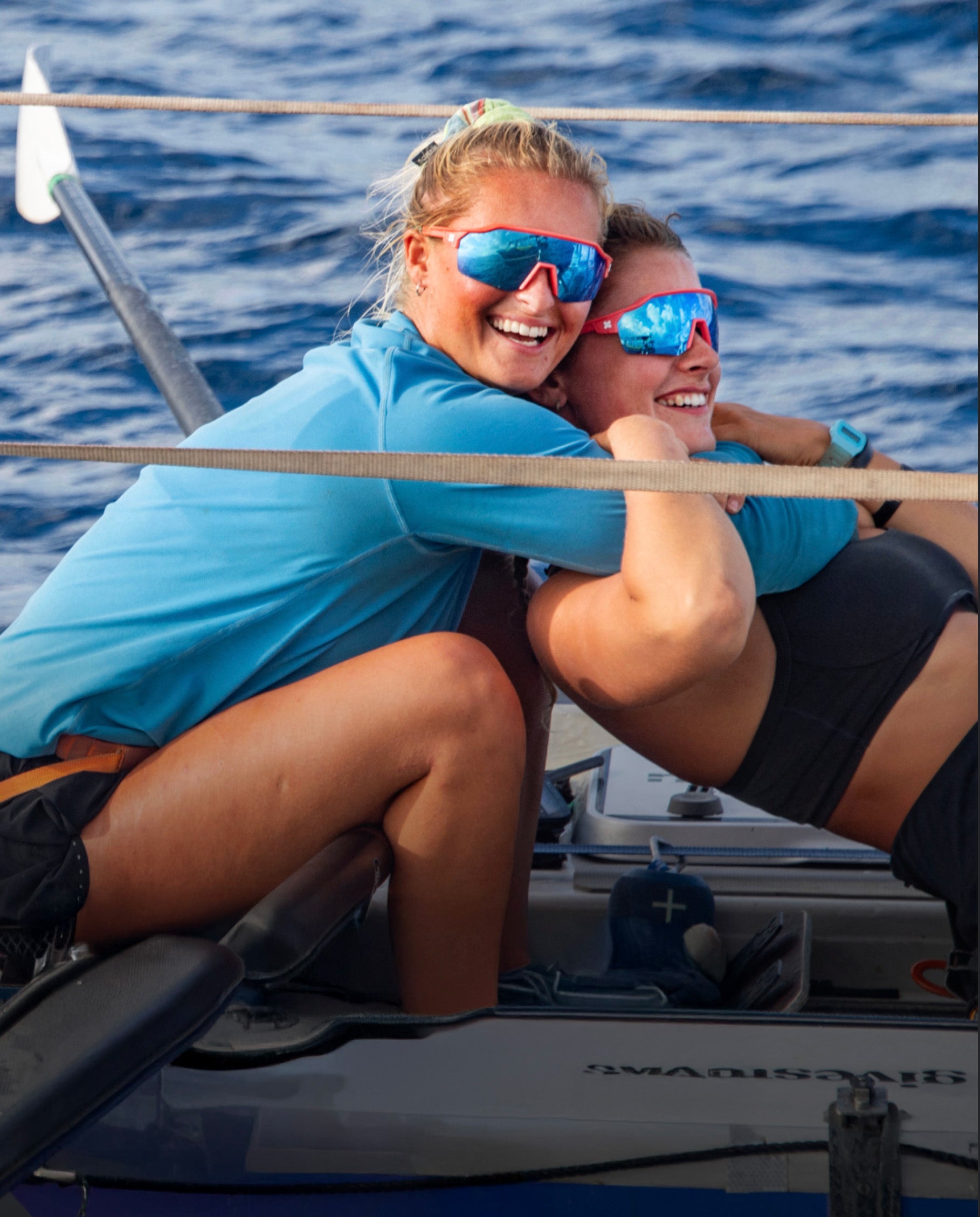 Two people on a boat wearing blue sunglasses with a blue water background